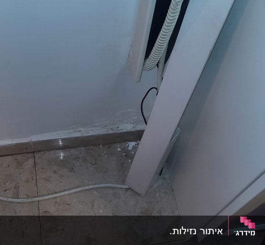 כבל חשמל על רצפה ליד קיר עם סימני רטיבות